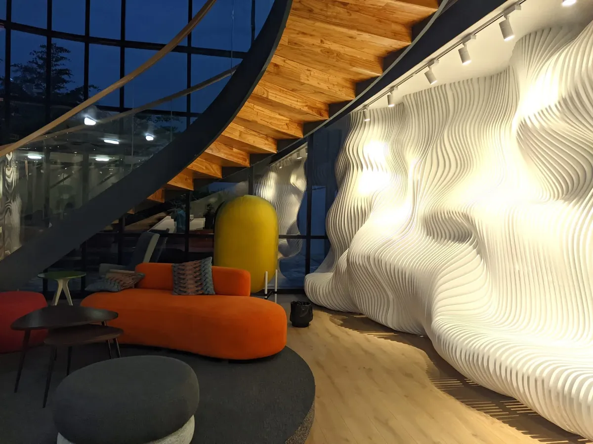 A studio space with a sculpted white wall, a wooden staircase and an orange sofa